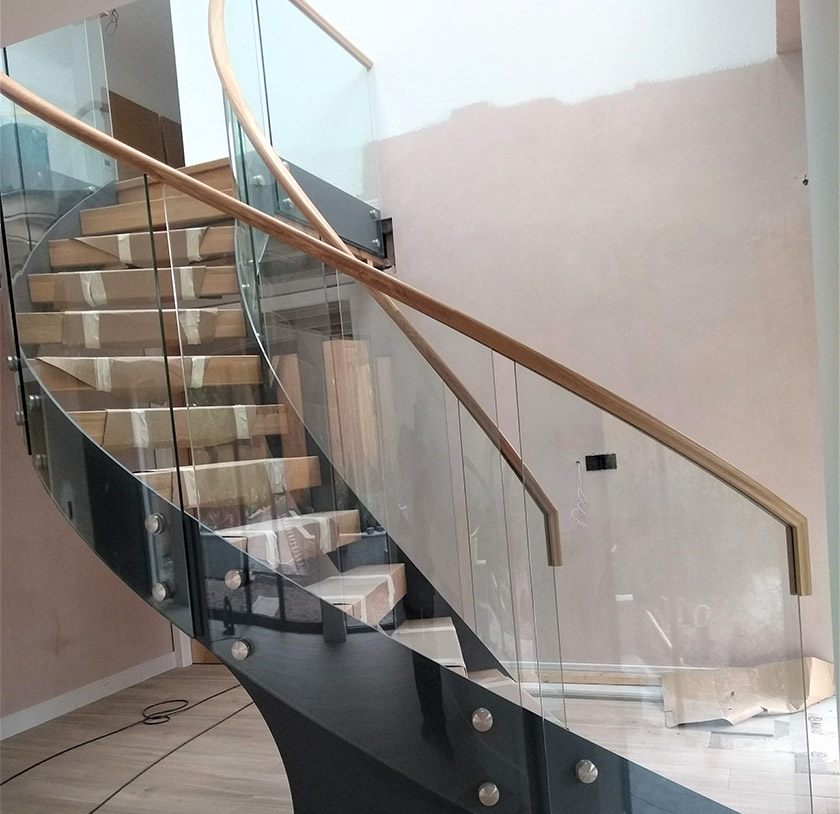Curved glass balustrade with wooden banister around spiral staircase