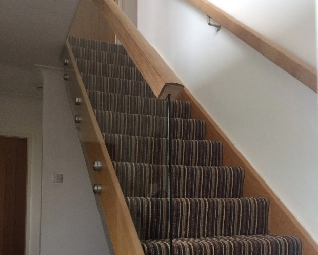 Glass balustrade with wooden banister next to carpeted staircase