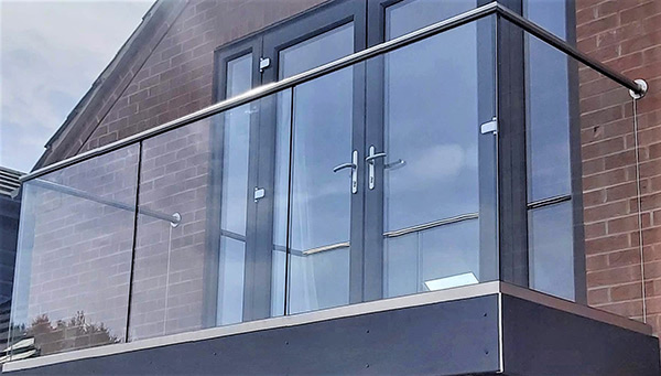 Glass balustrade with stainless steel rail around an upper floor balcony in front of double doors