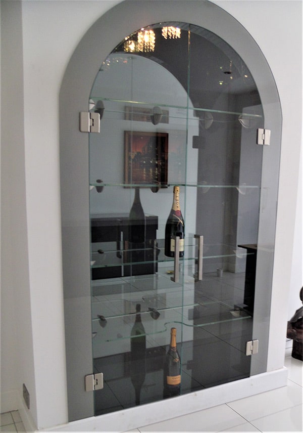 Glass shelving and doors in an alcove displaying wine bottles