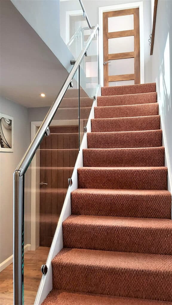 Glass balustrade with stainless steel banister next to carpeted staircase
